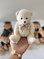 Small teddy bear held in a hand with other teddy bears in the background on a white surface.