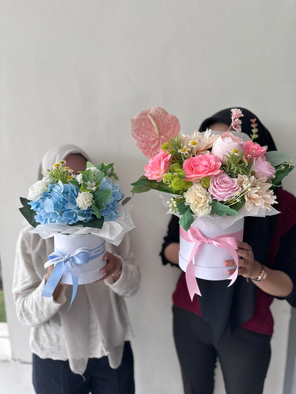 Two people holding flower bouquets against a plain background